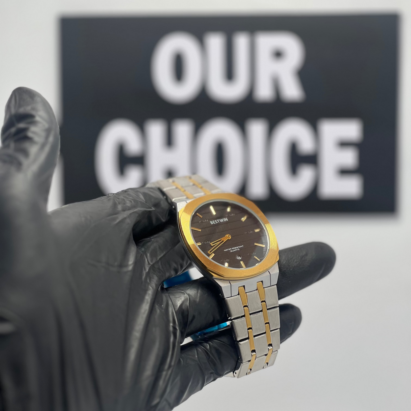 Gold and silver watch held by a gloved hand with 'OUR CHOICE' sign in the background